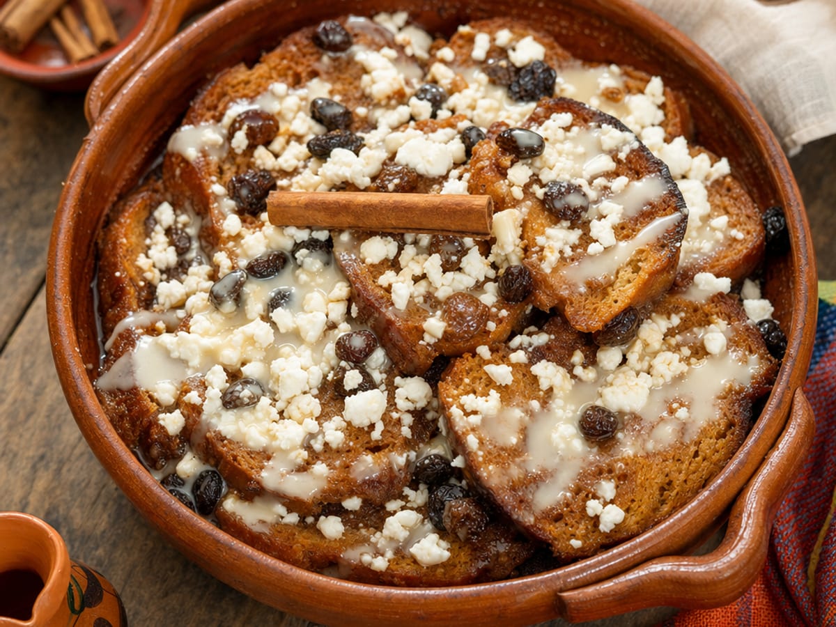 Capirotada mexicana en molde de barro con pan tostado bañado en miel de piloncillo, queso fresco y pasas